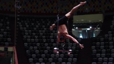Sirkin uçuş çubuğunda performans gösteren akrobatik bir adam destek olmadan baş aşağı dönüyor.