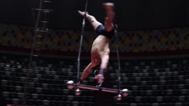 Sirkin uçuş çubuğunda performans gösteren akrobatik bir adam desteksiz dönüyor.