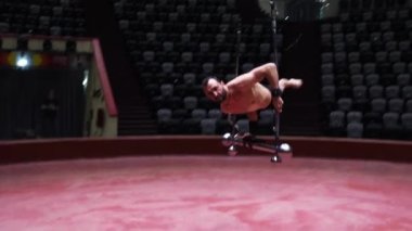 Parlak ışıklarla sirkin uçuş çubuğunda performansını sergileyen akrobatik bir adam havada bara çıkıyor.