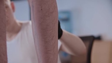 Genç bir adam, kuafördeki müşterisinin bacağındaki eliyle dövme çiziyor.