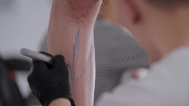 Jongeman tekent een schets voor tatoeage op het been van zijn cliënt in de salon — Stockvideo