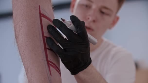 Unge man ritar en skiss för tatuering vid handen på benet med en röd markör — Stockvideo
