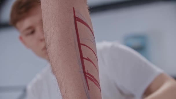 若い男は赤いマーカーで足に入れ墨のためのスケッチを描く — ストック動画