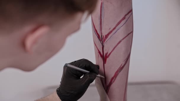 Jeune homme tatoueur dessiner un croquis sur la jambe sur son client avec un stylo — Video