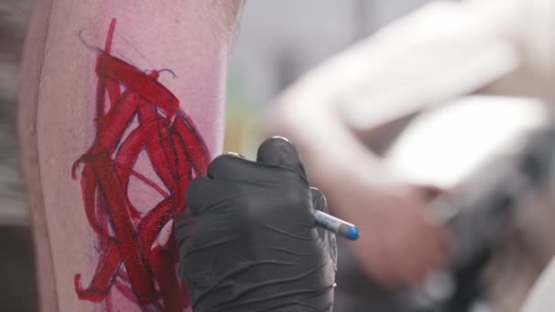 若いです男入れ墨アーティスト描いているスケッチ上の彼のクライアント上のペンで彼のクライアント上の赤いマーカー — ストック動画