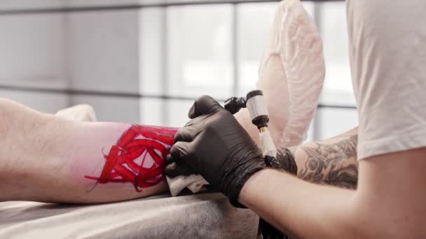 Giovane tatuatore inizia a tatuare sulla gamba del suo cliente — Video Stock