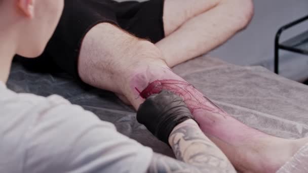 Un uomo che fa una sessione nel salone del tatuaggio - facendo un tatuaggio sulla gamba — Video Stock