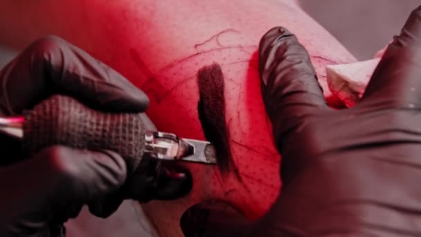 Una sesión en el salón de tatuajes: rellenar el tatuaje con color negro bajo la luz roja — Vídeos de Stock