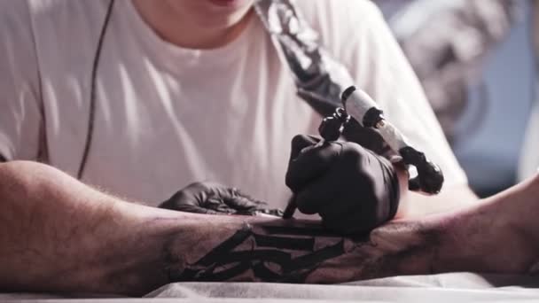 Uma sessão no salão de tatuagem - jovem tatuando letras grandes na perna - olhando para a câmera — Vídeo de Stock