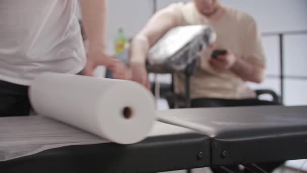 Getatoeëerde man bereidt de plaats voor zijn werk voor - bekleding van de stoel met wegwerp laken — Stockvideo