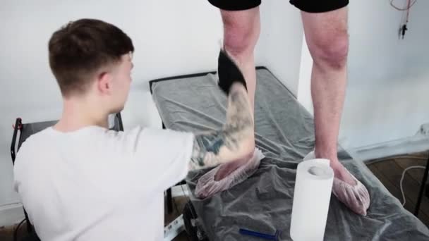 문신 전문가인 타투살 론 - 면도 크림에서 고객의 다리를 걷어 내는 모습 — 비디오