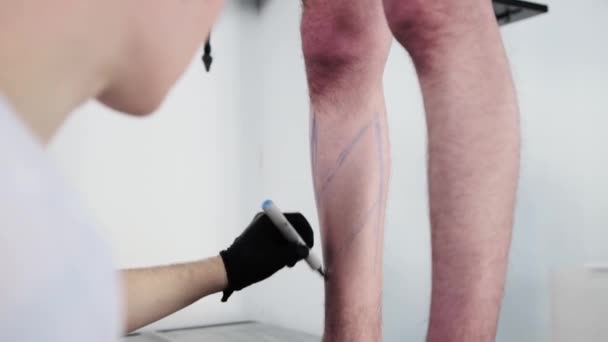 Tetovací salon - mladý muž tetování mistr kreslení náčrtek na noze s modrou značkou — Stock video