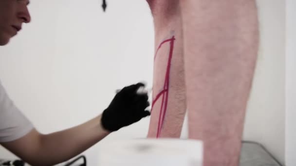 Tatuering salong - ung man tatuering mästare rita en skiss på benet med röd markör — Stockvideo