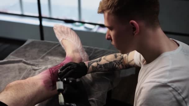 Tattoo session in salon - client lying on the couch and getting a big tattoo on his leg — Vídeo de Stock