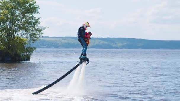 KAZAN, RÚSSIA 21-05-21: homem esportivo com um menino em um flyboard sobre o rio com uma ilha em um fundo — Vídeo de Stock