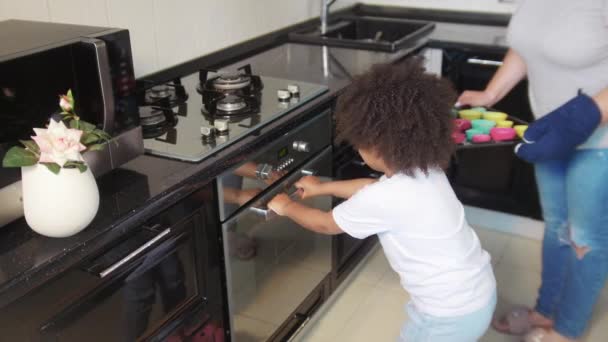 家庭烘焙- -一个黑人小女孩和她的白人妈妈在厨房做蛋糕- -把蛋糕放在烤箱里 — 图库视频影像