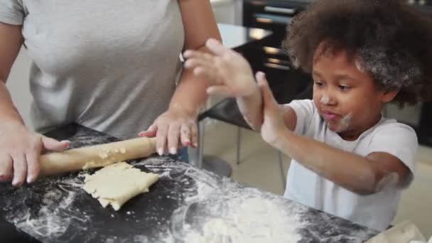 Assar em família - menina negra e sua mãe fazendo cupcakes na cozinha - a menina coberta de farinha e tentando sacudi-lo — Vídeo de Stock