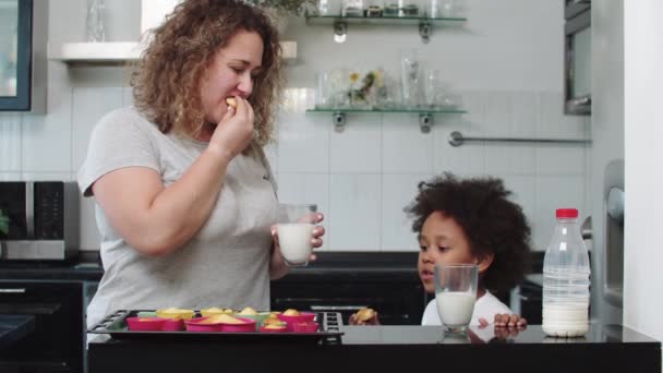 Madre blanca con su hija negra mixta comiendo cupcakes con leche — Vídeos de Stock