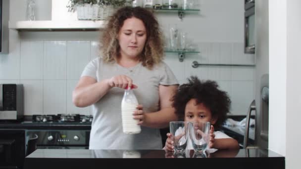 Beyaz anne ve melez siyah kızı mutfakta. Bardağa süt döken kadın. — Stok video