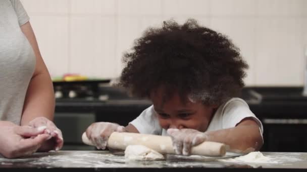 Fekete kislány az anyjával, aki a konyhában teríti ki a dohányt. — Stock videók
