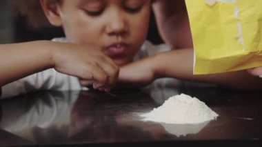 Masaya un dökülürken küçük siyah bir kız bakıyor.