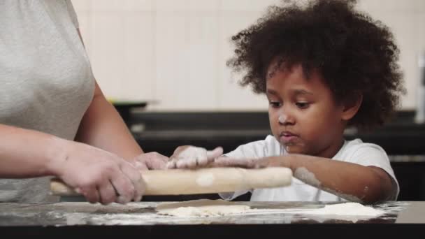 Negro niña sonriente con su madre rodando la masa en la cocina brillante — Vídeos de Stock