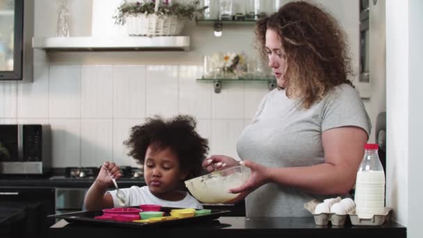 Familia mixta haciendo cupcakes - verter masa líquida cruda en los moldes de pastel con una cuchara — Vídeos de Stock