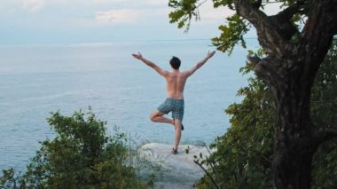 Sabahın erken saatlerinde uçurumda yoga egzersizleri yapan genç bir adam.