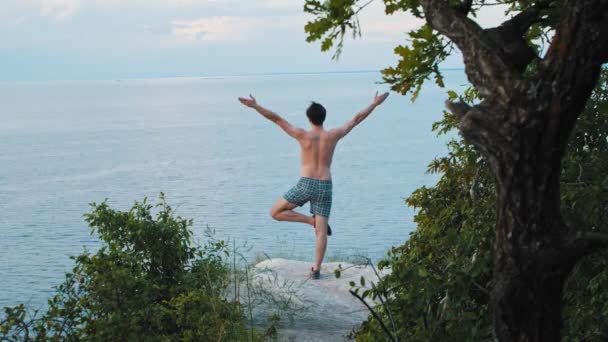 Young man doing yoga exercises on the cliff in early morning — Stock Video