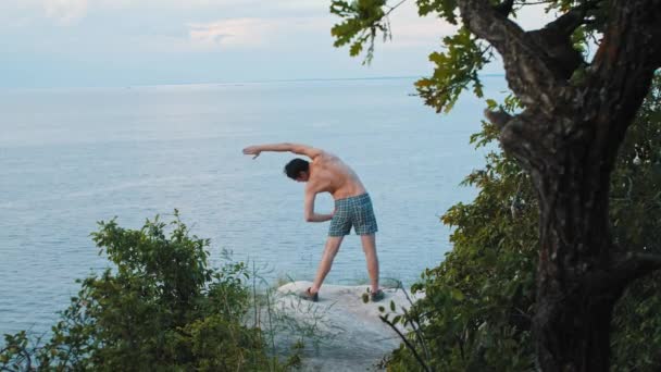 Pemuda yang melakukan latihan olahraga di tebing di pagi hari membungkuk ke samping — Stok Video