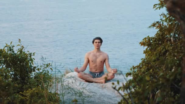 A young shirtless man meditates on a mountain in the early morning — Stock Video