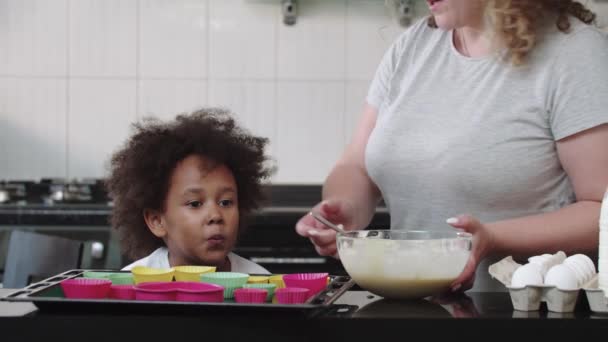 Uma menina negra comendo massa líquida crua com uma colher enquanto sua mãe se afasta — Vídeo de Stock