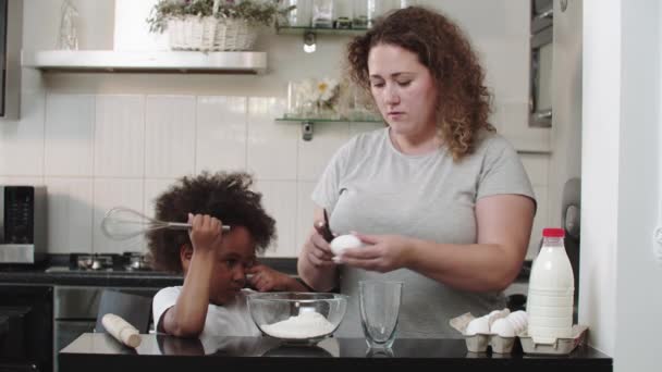 Cuisson familiale mixte - maman brise un œuf dans un bol en verre pour la pâte — Video