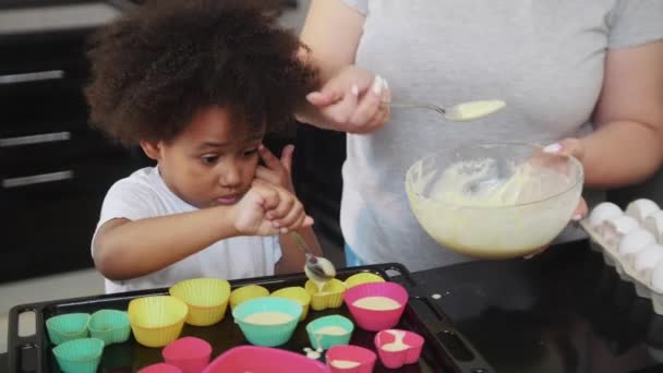 Petite fille noire avec sa mère blanche dépose la pâte dans les petits moules à gâteau — Video