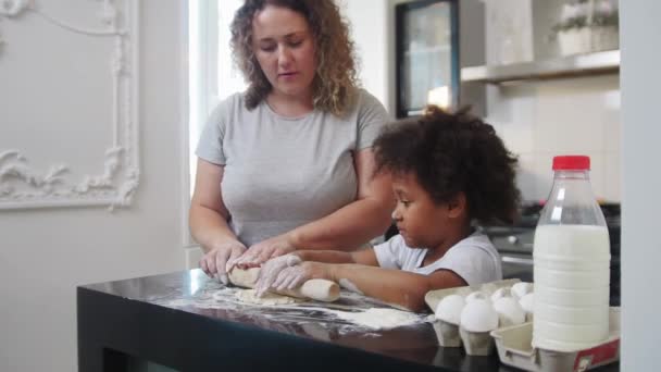 Cuisson familiale - petite fille noire et sa mère blanche déroulant la pâte avec une corde à sauter — Video
