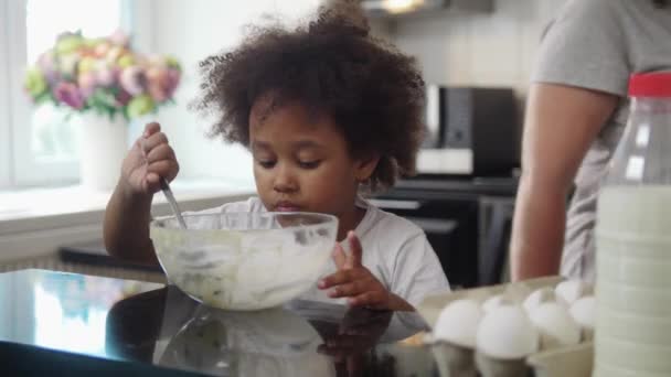 Hornear en familia - niña negra comiendo los restos de una masa líquida del tazón — Vídeos de Stock