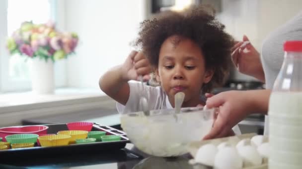 Familienbacken - afrikanisch-amerikanisches kleines Mädchen isst die Reste eines flüssigen Teigs aus der Schüssel — Stockvideo