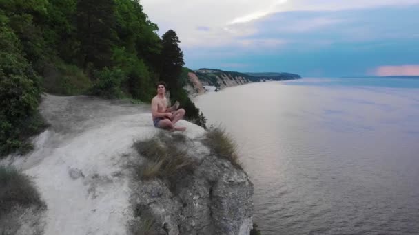 Ung skjorta man spelar ukulele på klippan runt skogen och floden tidigt på morgonen — Stockvideo