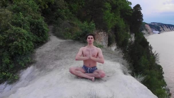 Молодой человек без рубашки медитирует на утесе рано утром — стоковое видео