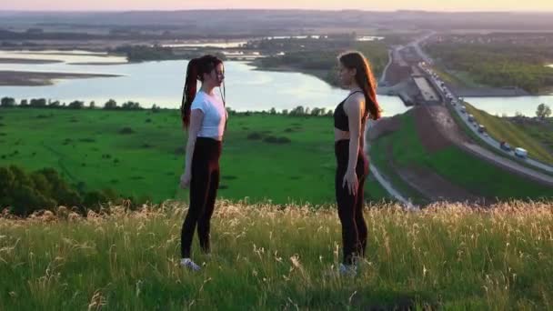 Две молодые женщины делают упражнения на корточках на поле — стоковое видео