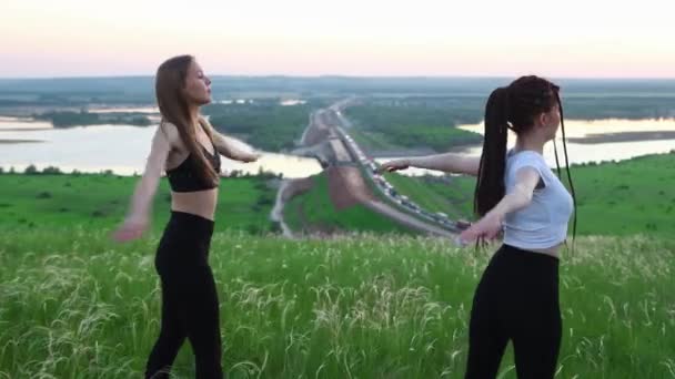 Две молодые женщины делают упражнения на зеленом поле во время позднего заката — стоковое видео