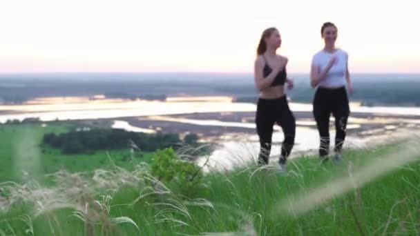 Dos mujeres jóvenes en ropa deportiva corriendo por el campo y se sienta en la hierba — Vídeo de stock