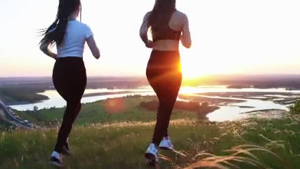 To unge kvinder i sportstøj jogger rundt på marken ved solnedgang – Stock-video