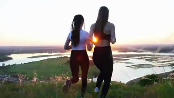 Dos mujeres jóvenes con ropa deportiva trotando en el campo al atardecer — Vídeos de Stock