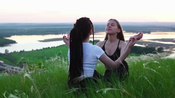 Dos mujeres jóvenes sentadas en la hierba y tratando de meditar — Vídeos de Stock