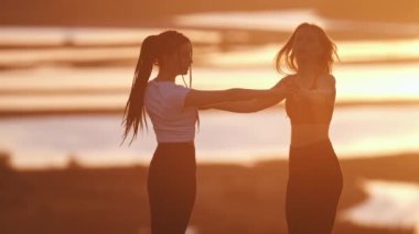 Gün batımında vinç pozisyonunda duran iki genç kadın.