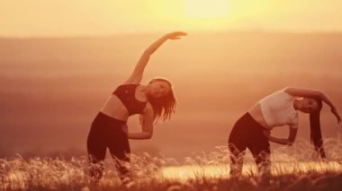 Gün batımı sahasında esneme egzersizleri yapan iki genç kadın.