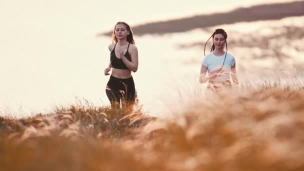Две девушки бегают по пшеничному полю на закате — стоковое видео
