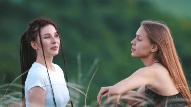 İki genç güzel kadın çimenlerde oturup konuşuyor.