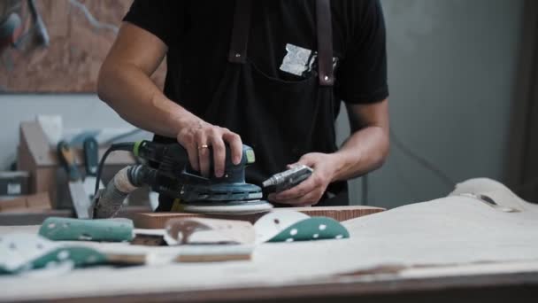 Mannenwerker die een houten stuk in de werkplaats slijpt met een instrument — Stockvideo